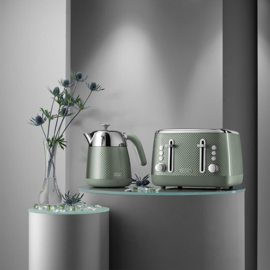 Green kettle and toaster on a glass shelf with a gray wall background
