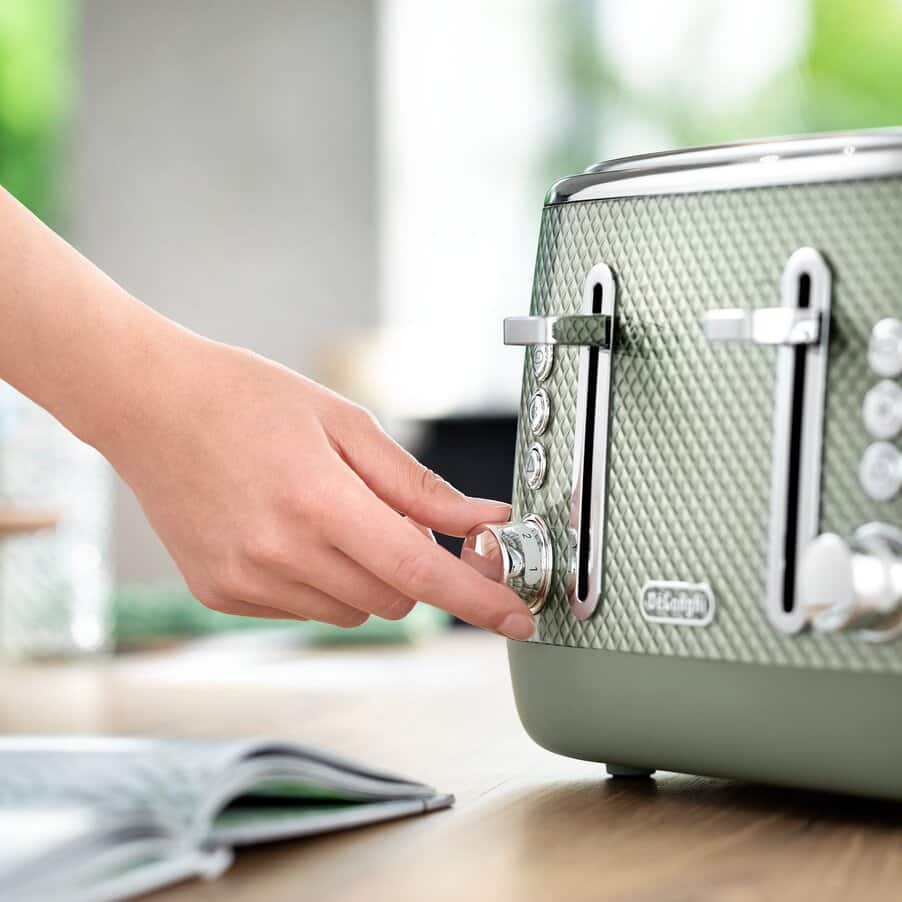 Person adjusting a green toaster on a kitchen counter